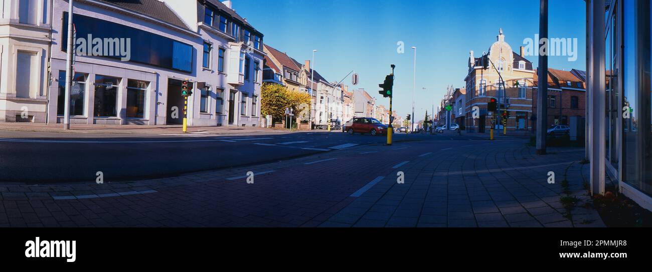 A panoramic view of a bustling city street; its built structures, crossroads and passing cars illuminated by traffic lights from a low angle. Stock Photo