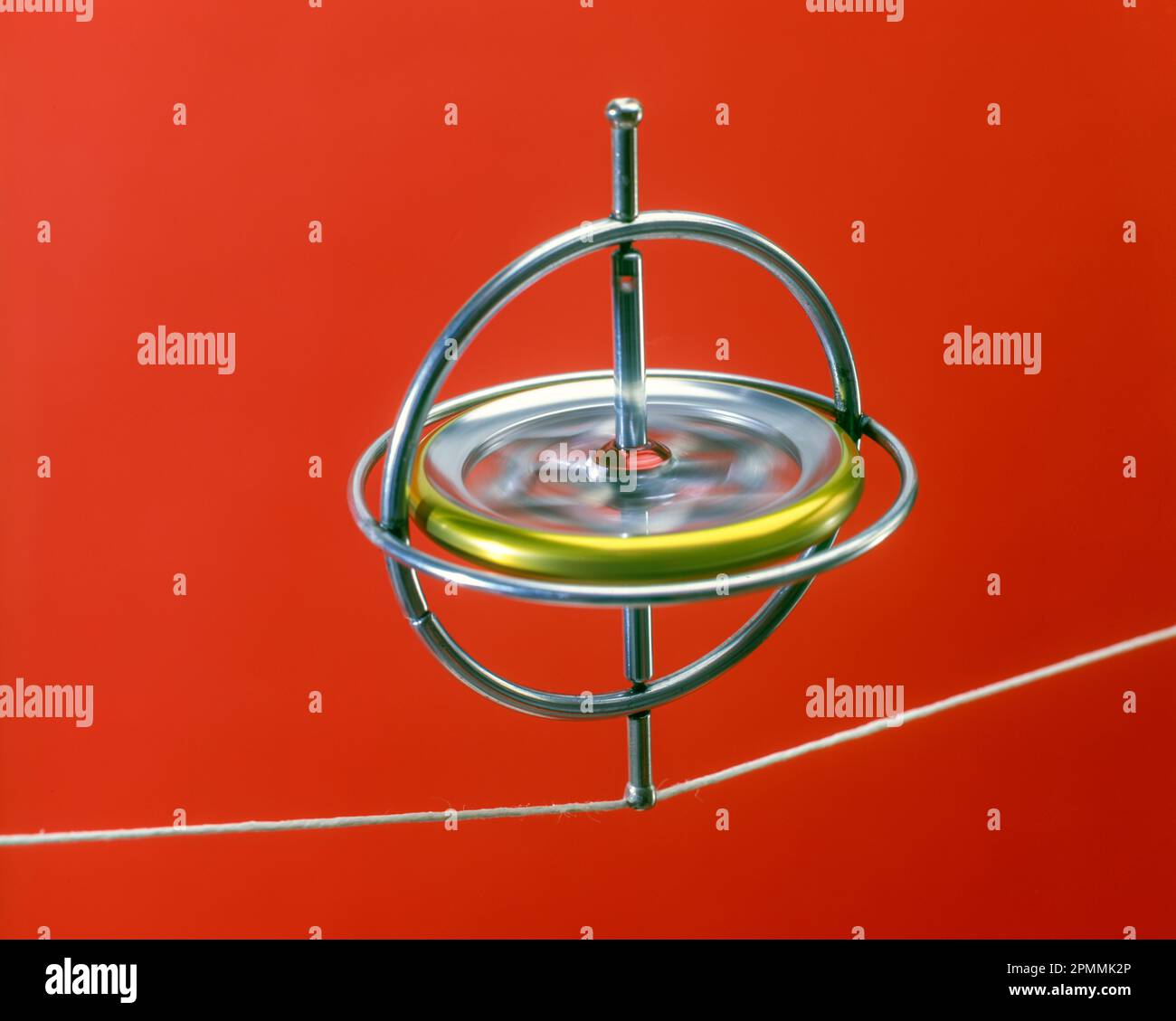 SPINNING WHEEL GYROSCOPE BALANCES SUSPENDED ON WHITE STRING ON RED BACKGROUND Stock Photo Alamy