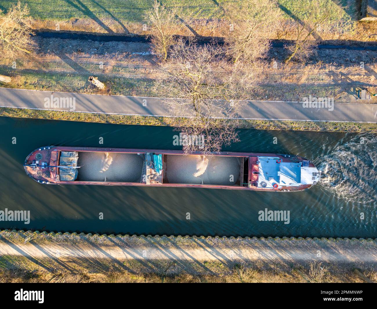 Aerial view from a drone of a cargo canal ship passes by over the canal on a sunny winter day, reflections are to be seen in the water, canal system in the outskirts of Rijkevorsel, Belgium. High quality photo Stock Photo