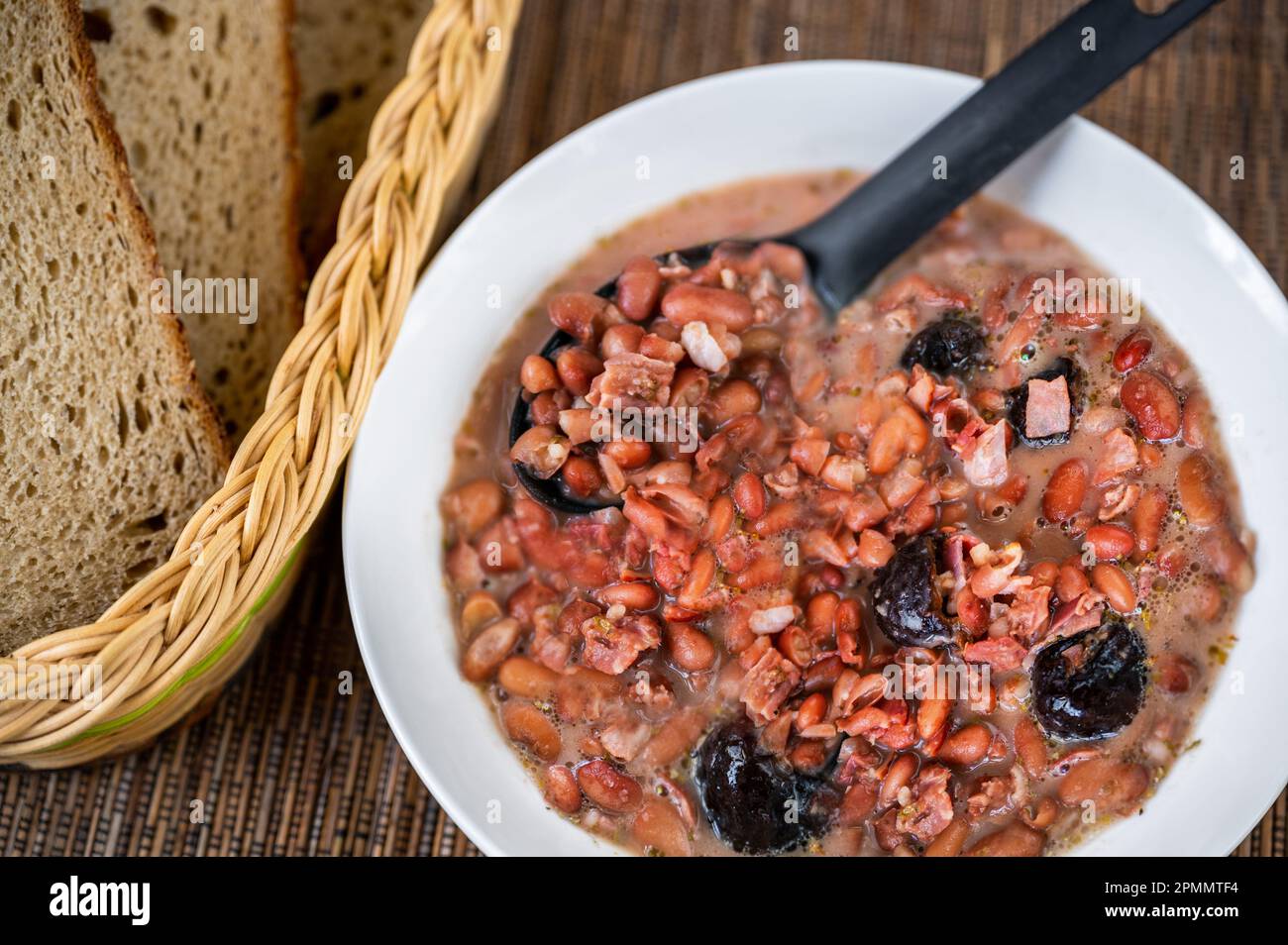 Legume soup from bean and plum in white plate, bread on table, closeup. Stock Photo