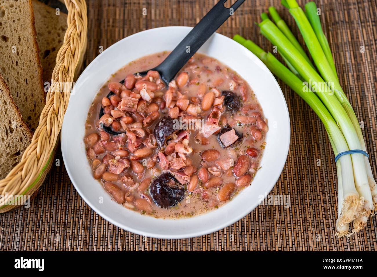 Legume soup from bean and plum in white plate, green onion, bread on table. Stock Photo