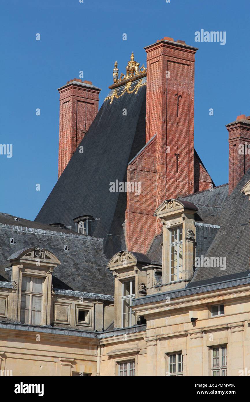 Fontainebleau Palace: the brick chimneys, steep-pitched slate-tiled roof and gold acroteria atop the medieval keep  seen from Place de la Fontaine Stock Photo