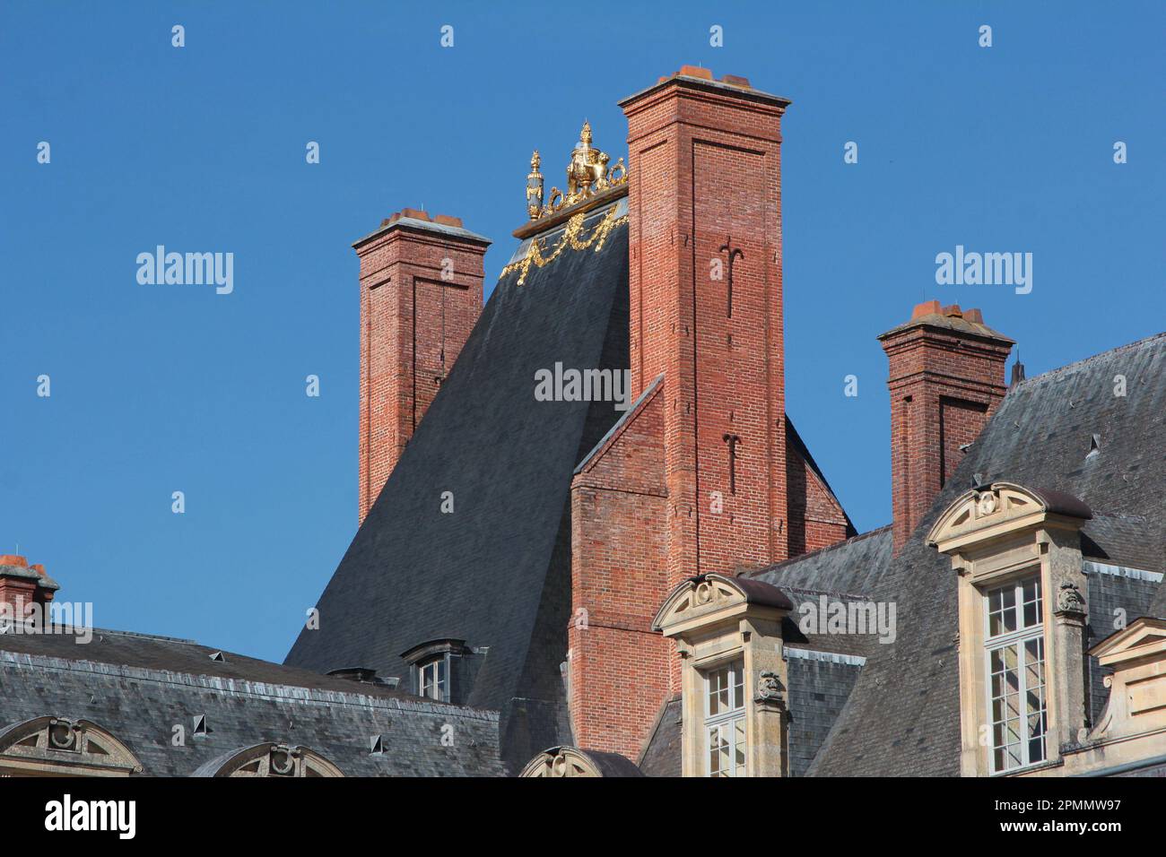 Fontainebleau Palace: the brick chimneys, steep-pitched slate-tiled roof and gold acroteria atop the medieval keep seen from Place de la Fontaine Stock Photo