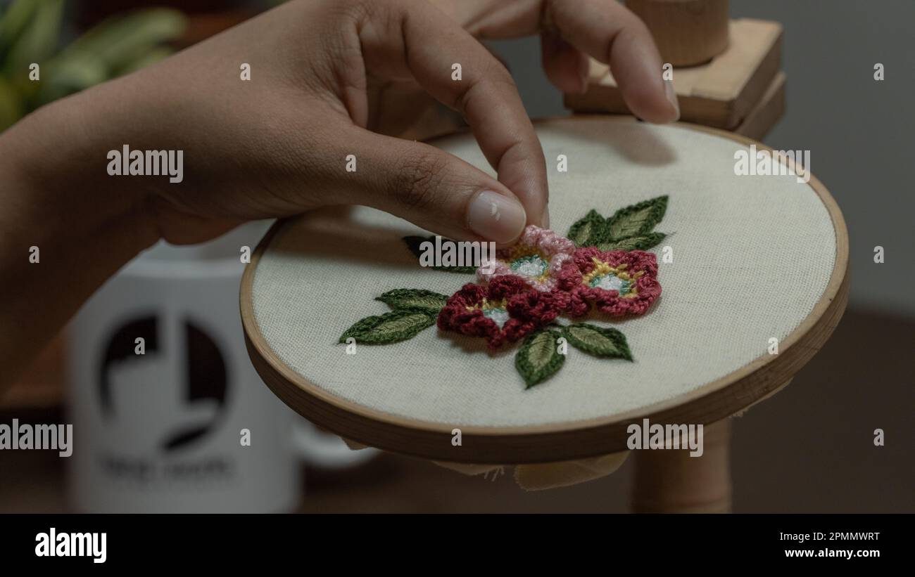 Woman's hands embroidering a flower on a wooden hoop. Stock Photo