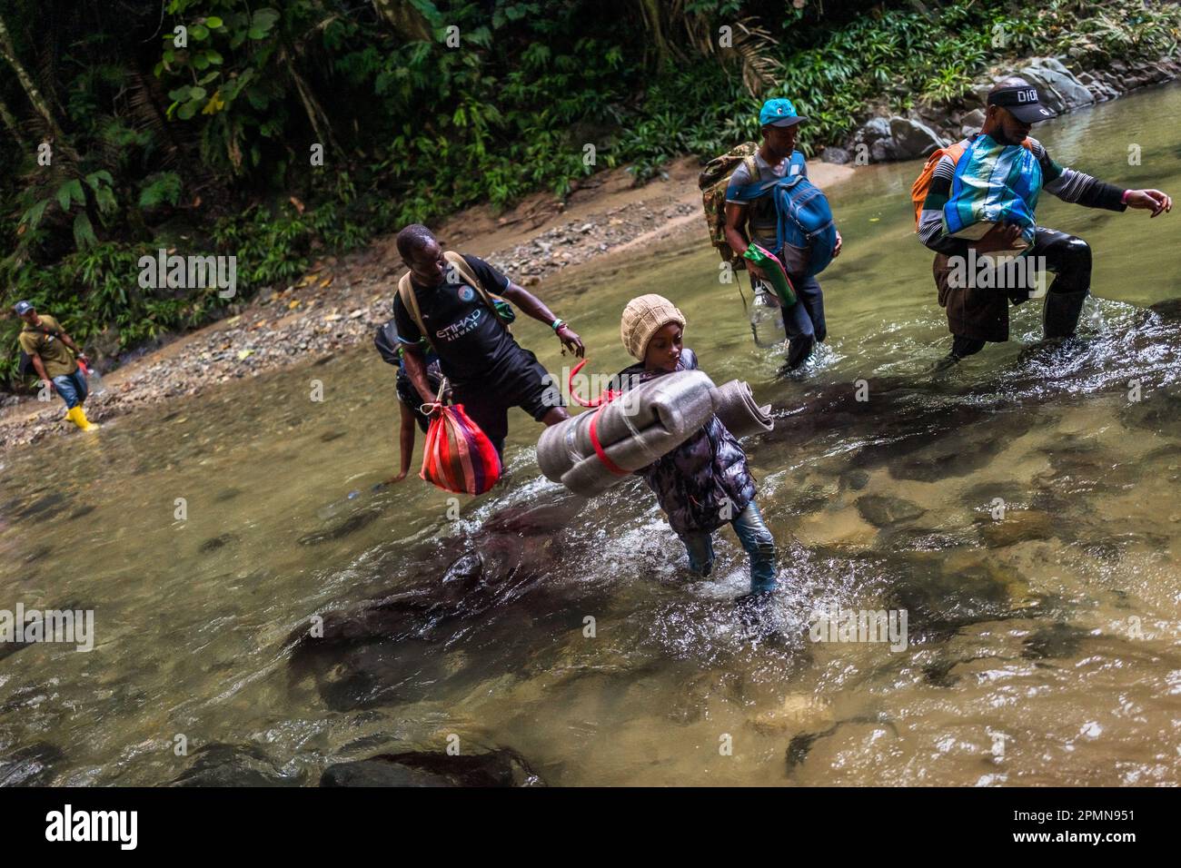 A Nigerian family of migrants walks through the river in the wild and dangerous jungle of the Darién Gap between Colombia and Panamá. Stock Photo