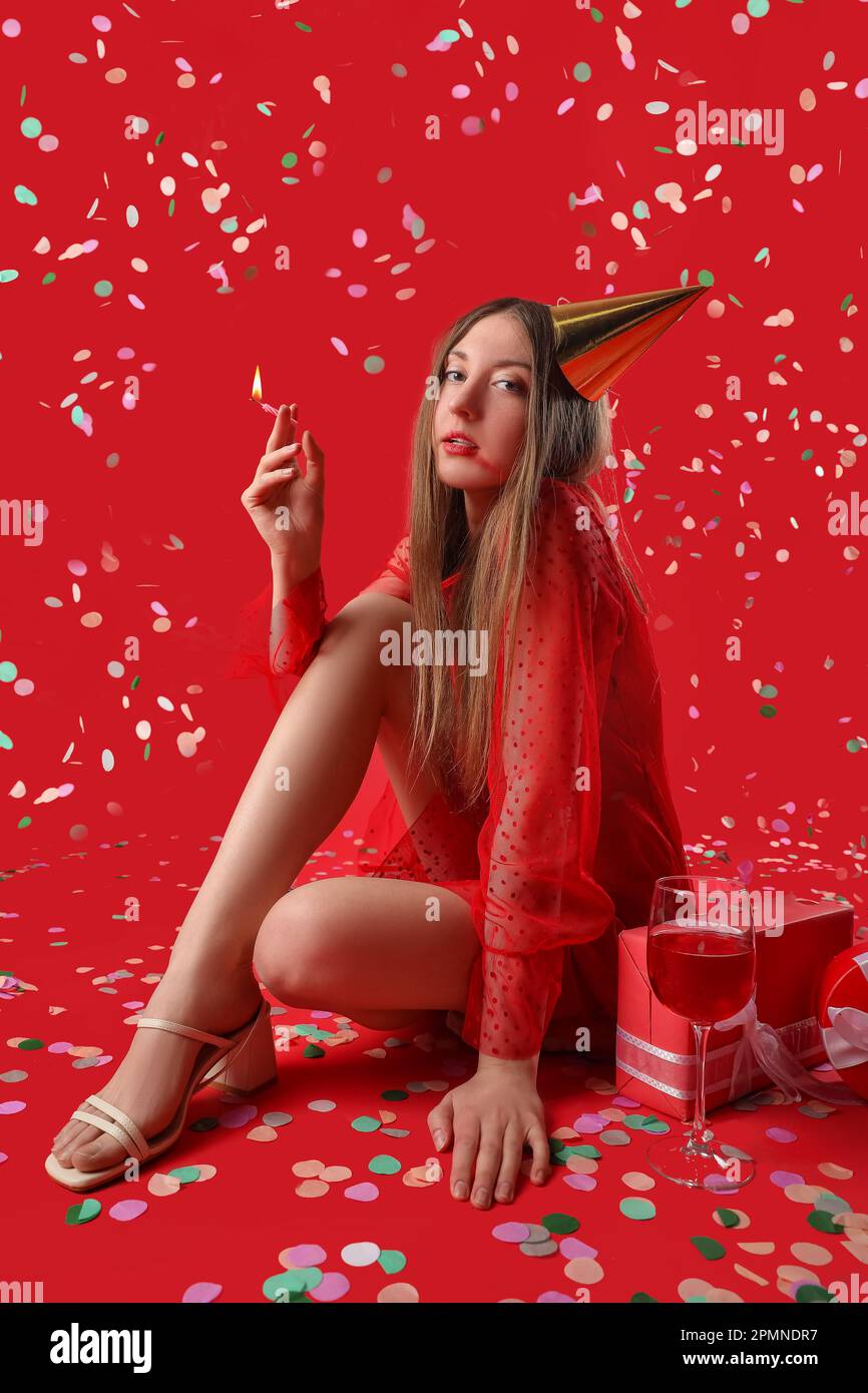 Drunk young woman with burning candle celebrating Birthday on red