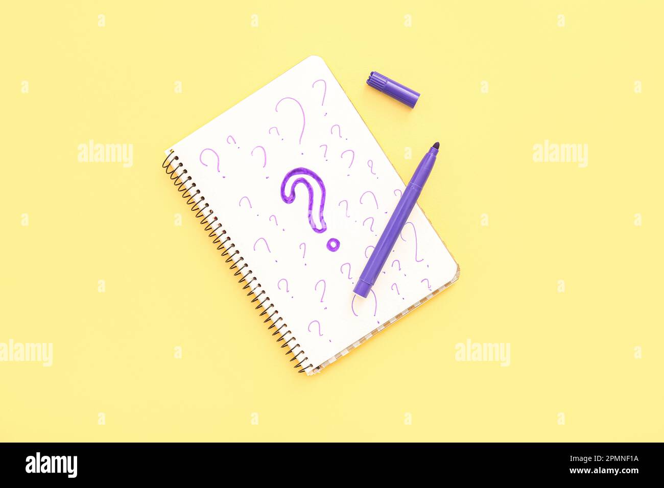 Notebook with drawn question marks and marker on yellow background Stock Photo