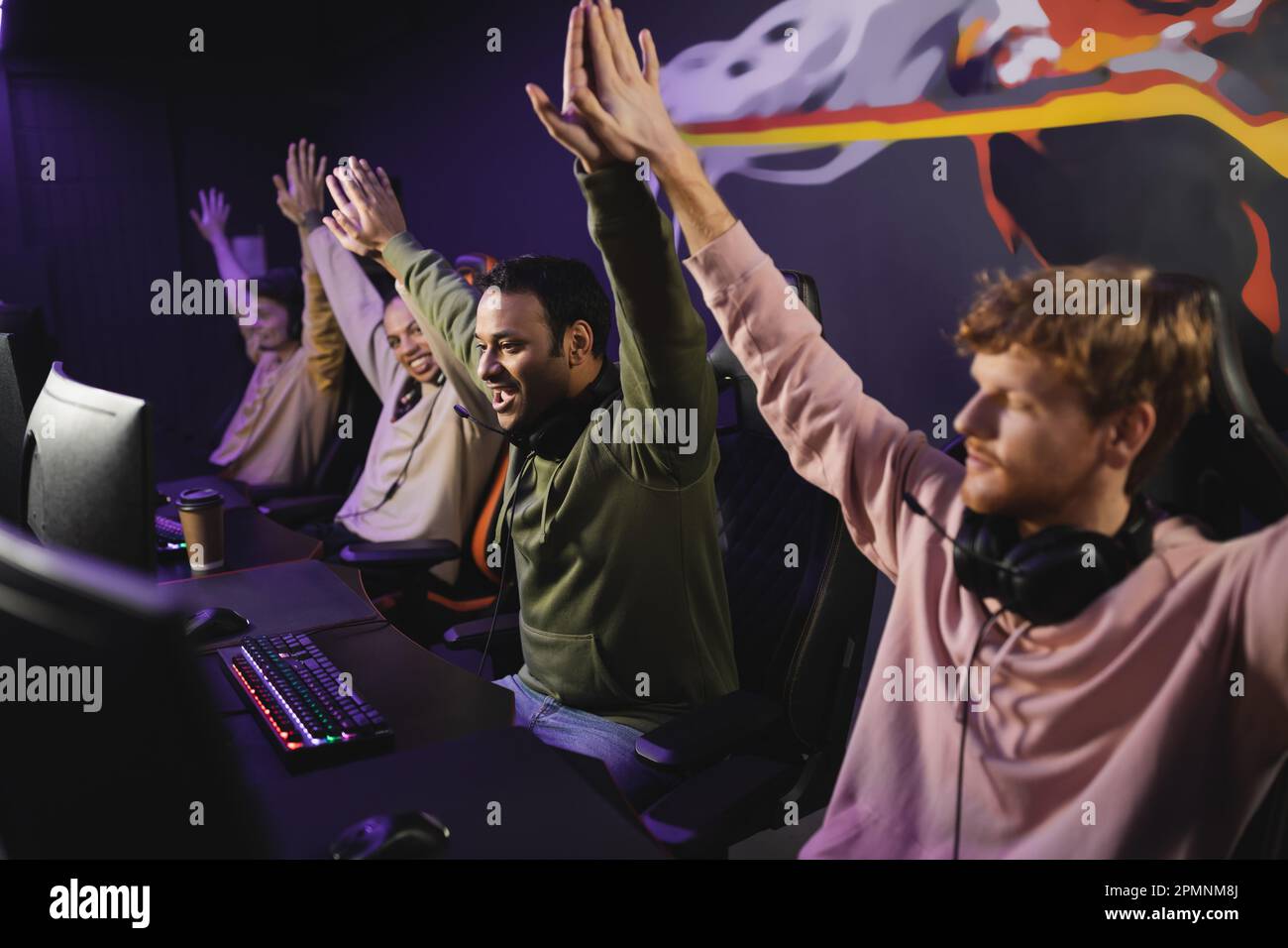 Excited indian man giving high five to friends near computers in gaming