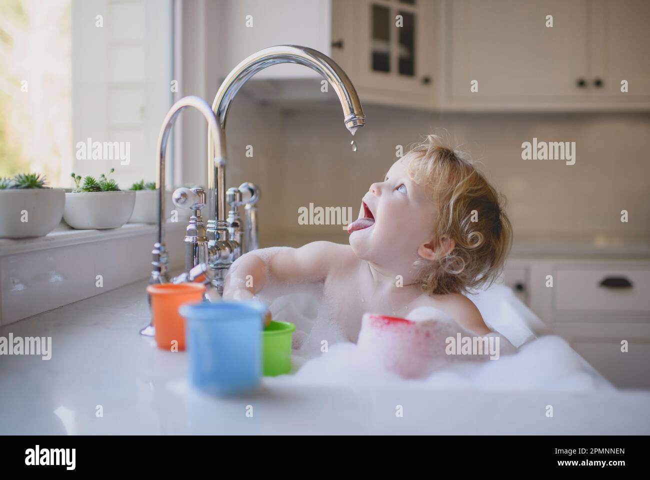 young toddler baby bathing in kitchen sink, bubbles in kitchen sink