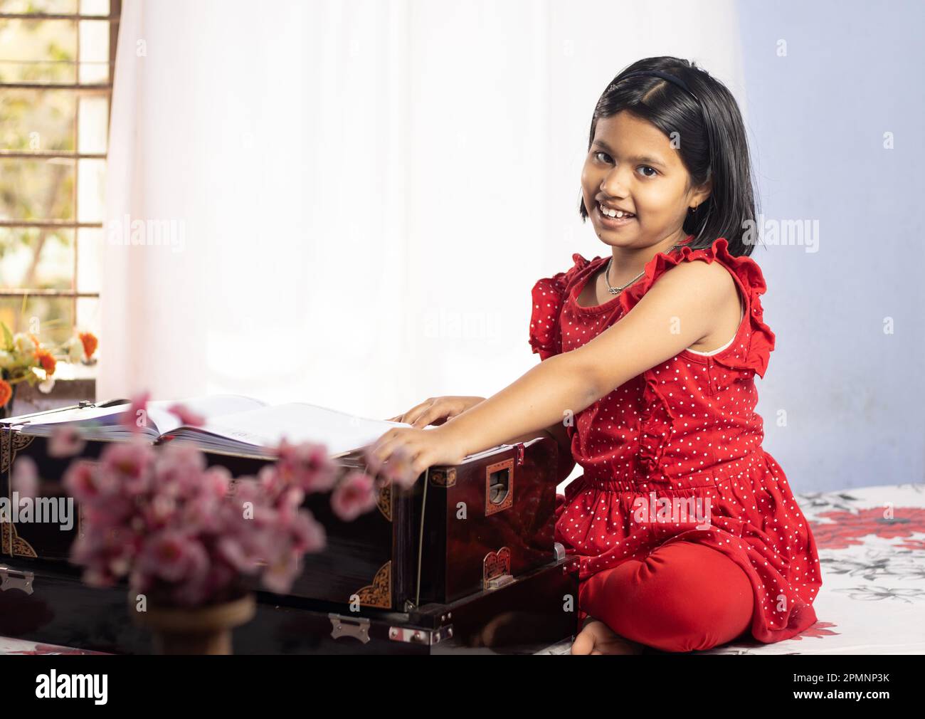 An Indian cute girl child singing and playing harmonium on white