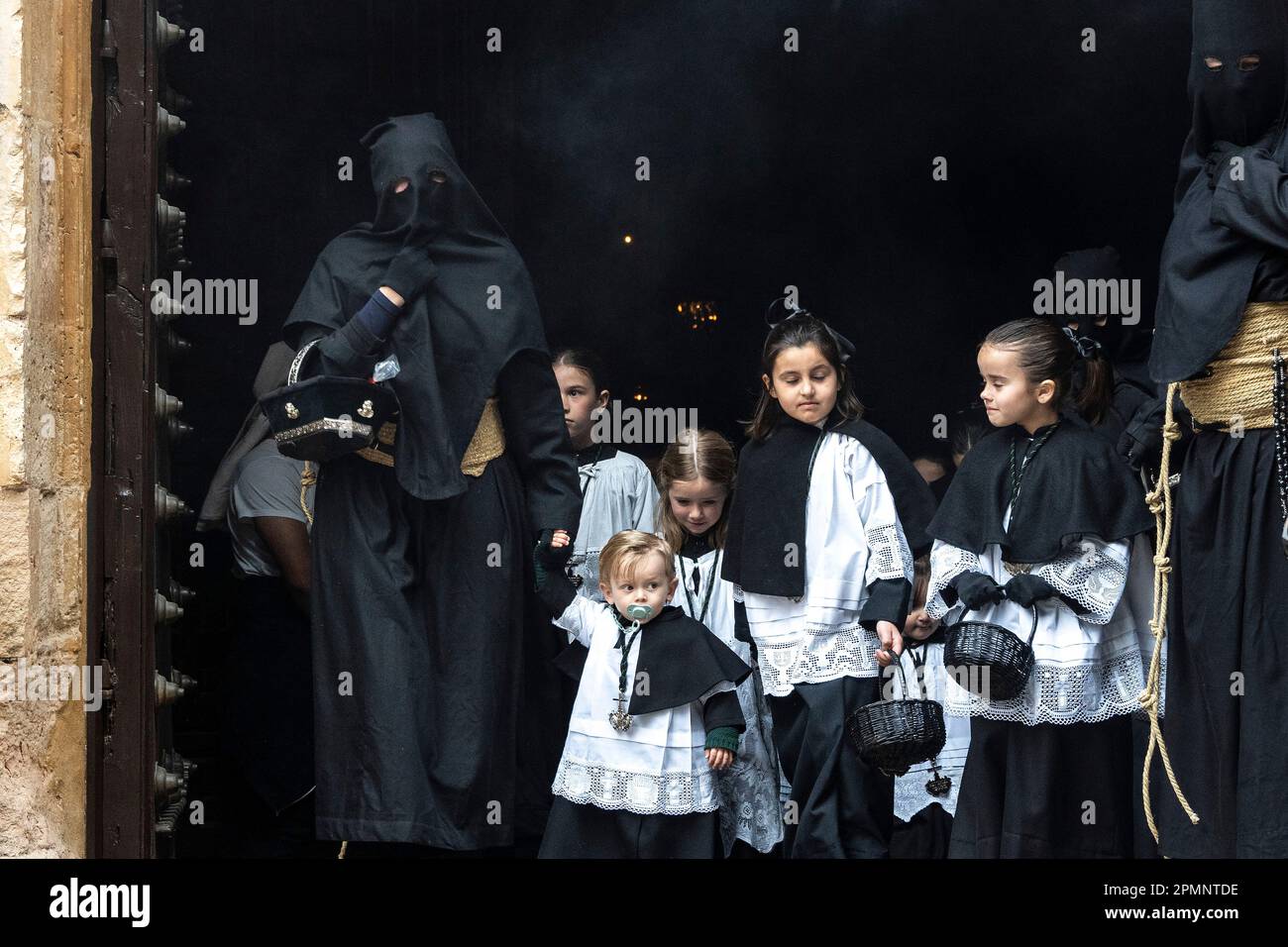 A penitent wearing black robes escorts young child as they depart from ...