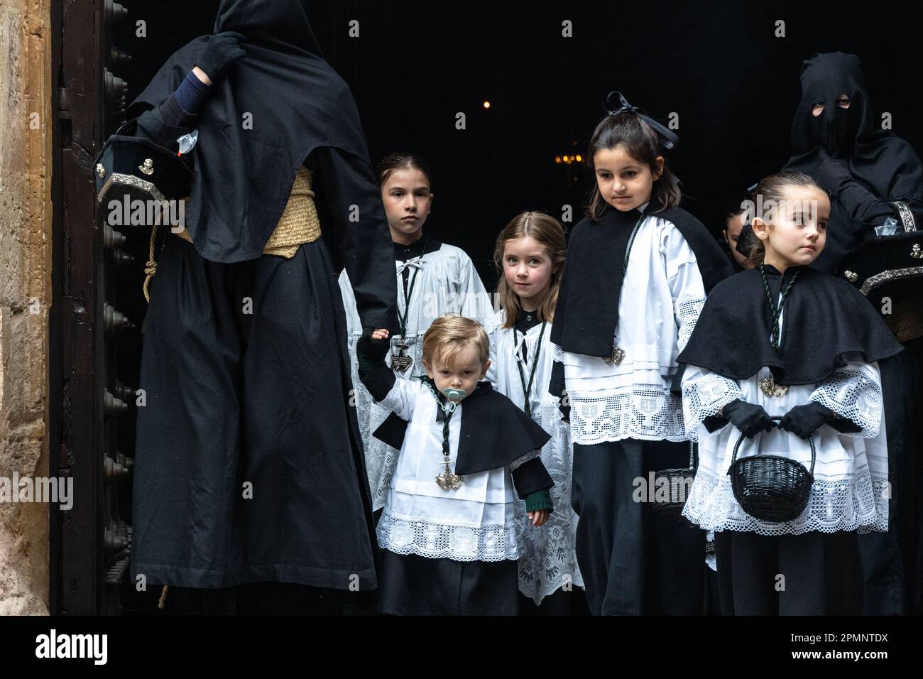 A penitent wearing black robes escorts young child as they depart from ...