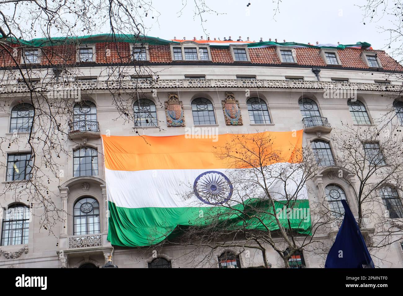 Diplomatic staff at the Indian High Commission wave a large tricolor on the roof as activists below protest the arrests of Sikhs in Punjab. Stock Photo