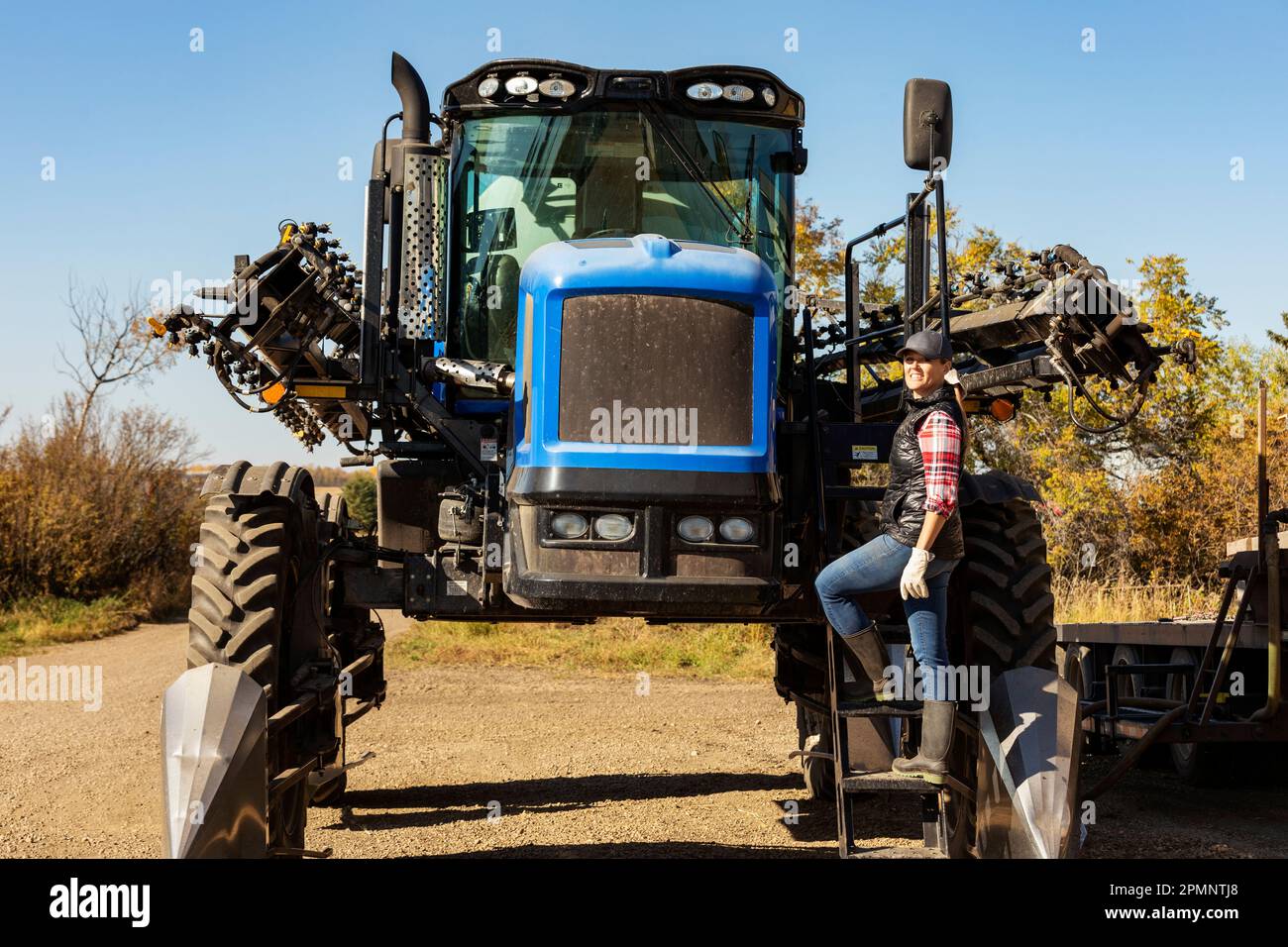 Portrait of a woman farmer standing on the steps of a tractor with seeder attachments; Alcomdale, Alberta, Canada Stock Photo