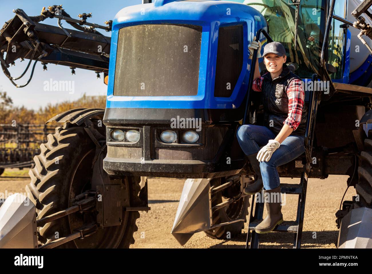 Portrait of a woman farmer sitting on the steps of a tractor with seeder attachments; Alcomdale, Alberta, Canada Stock Photo