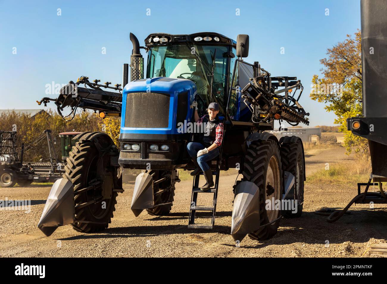 Portrait of a woman farmer sitting on the steps of a tractor with seeder attachments; Alcomdale, Alberta, Canada Stock Photo