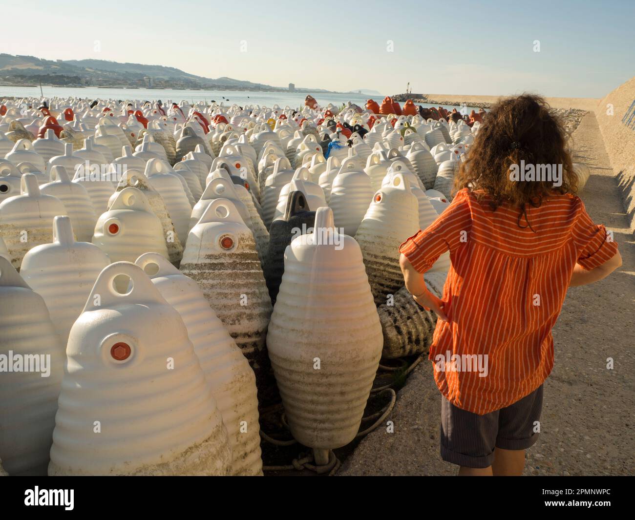 Large quantity of floats used for mussel cultures on the shore with hills in the background and a view from behind of a woman looking out to the se... Stock Photo