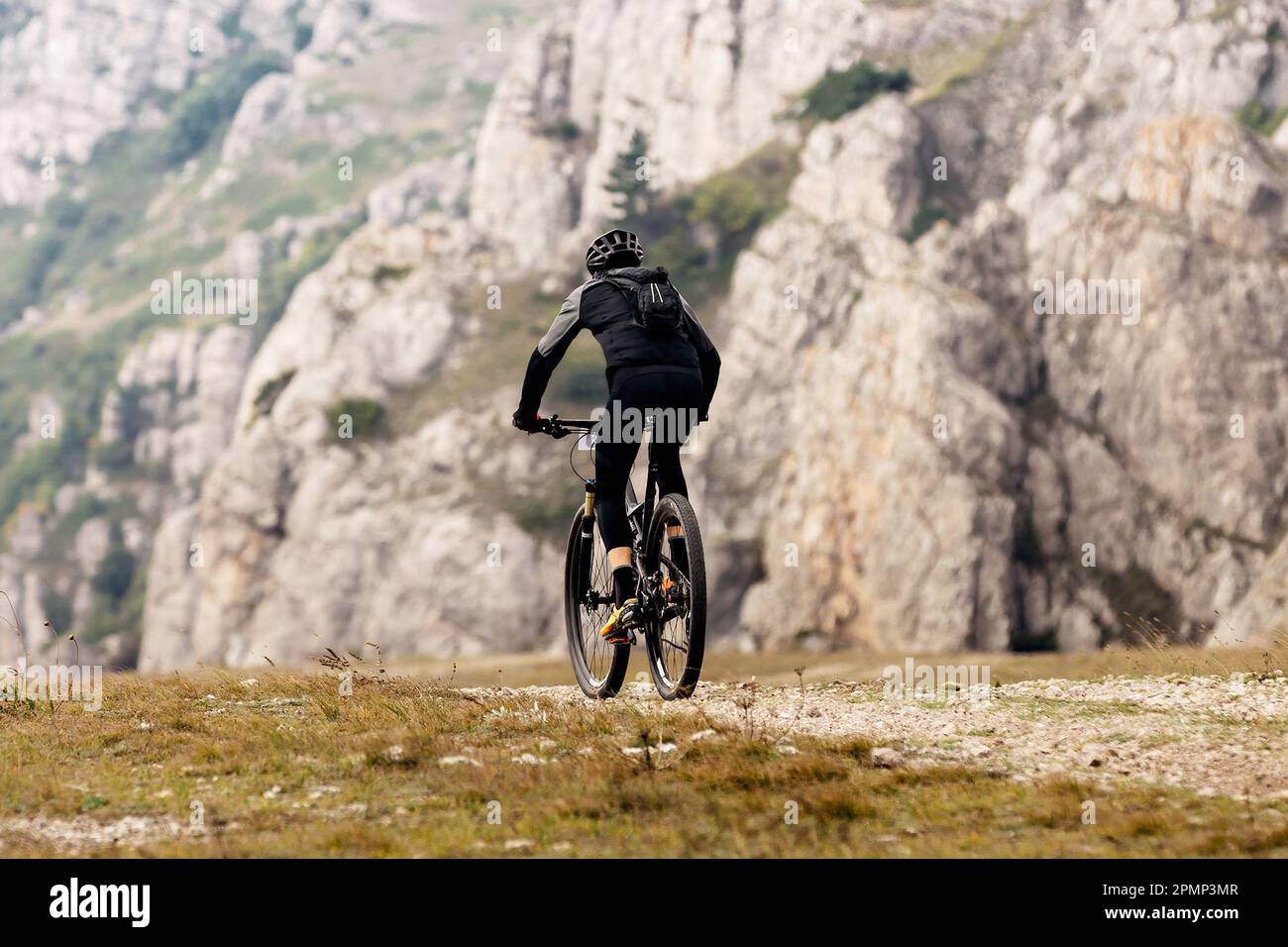 male cyclist riding mountain bicycle on mountainous region travelling cycling. backpack on back of mountain biker Stock Photo