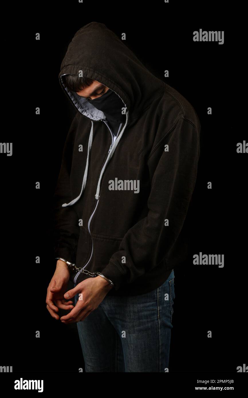 Arrested teenage boy in handcuffs wearing a mask and a hoodie Stock Photo