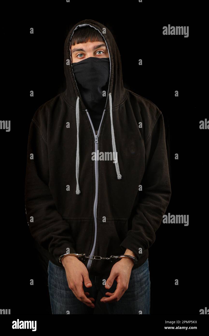 Arrested teenage boy in handcuffs wearing a mask and a hoodie Stock Photo