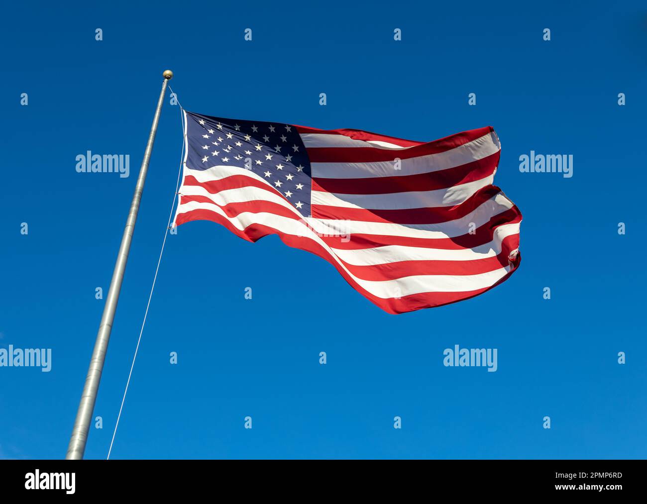Close up view of an American flag waving on a flagpole, with blue sky background Stock Photo