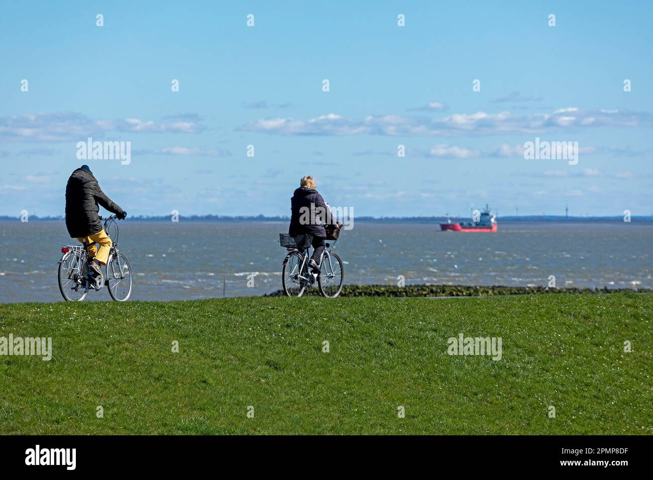 Cyclists, freight ship, dike, Cuxhaven, Lower-Saxony, Germany Stock Photo