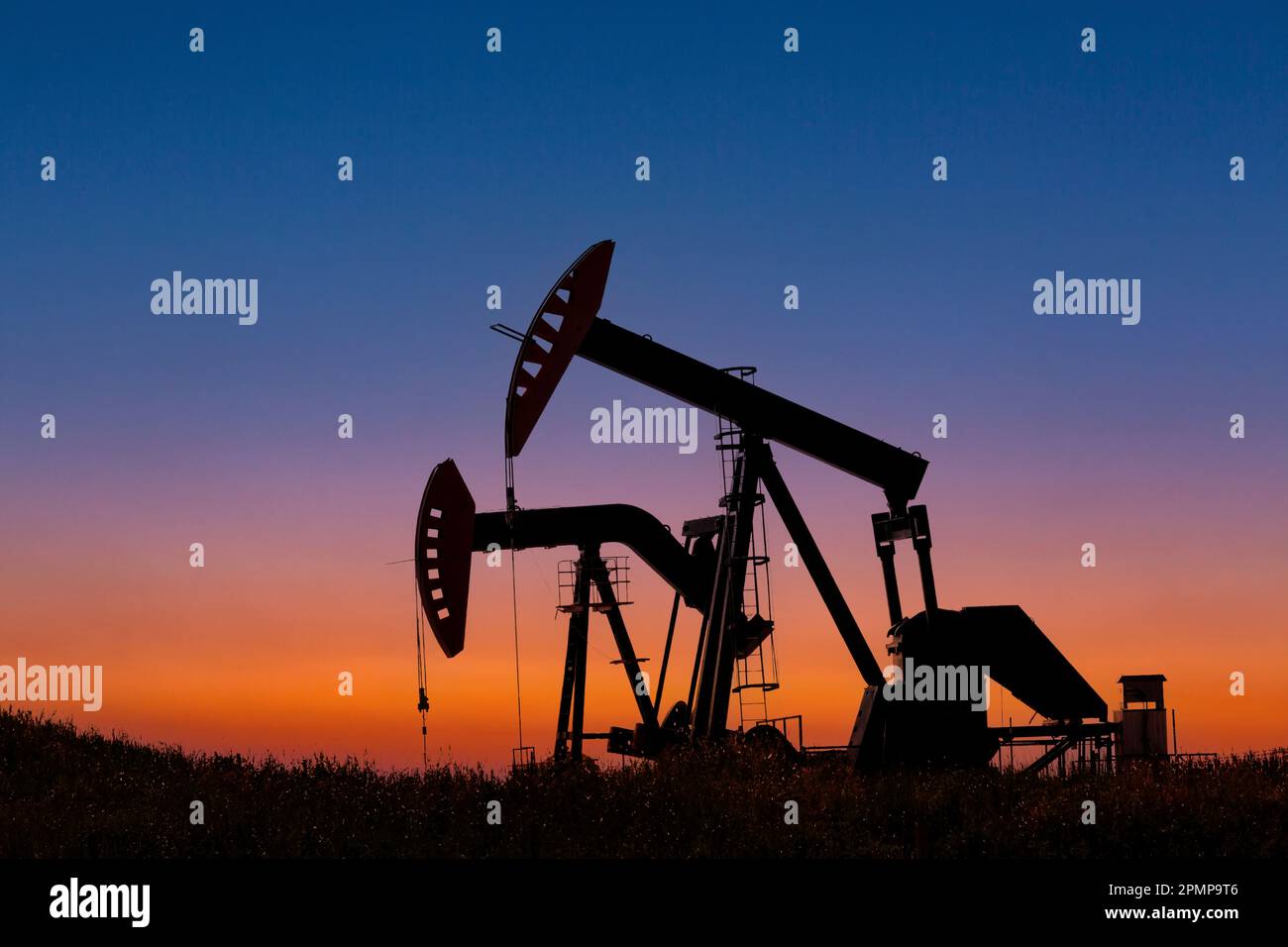 Silhouette of two pumpjacks at sunrise with glowing sky in the background, West of Airdrie; Alberta, Canada Stock Photo