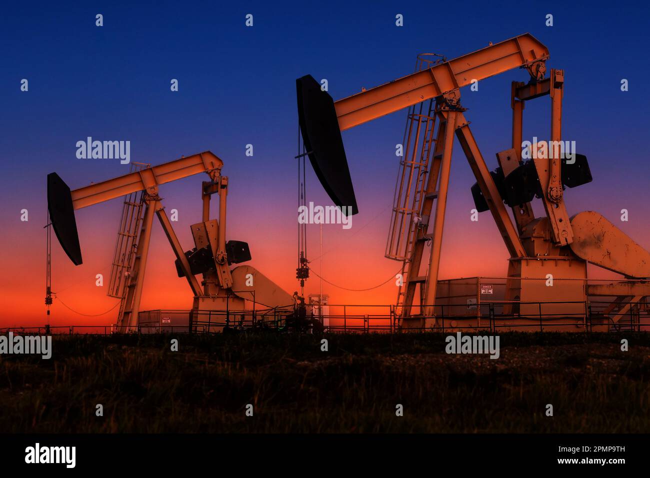 Glowing colourful pumpjacks at sunrise with glowing sky in the background, West of Airdrie; Alberta, Canada Stock Photo