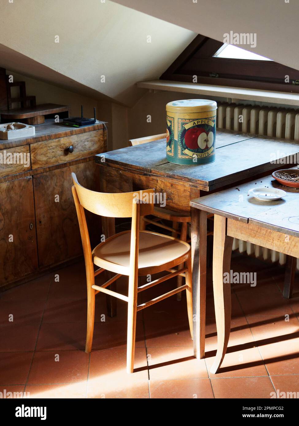 Table with novelty biscuit box in an attic room and wooden cupboard and chair Stock Photo