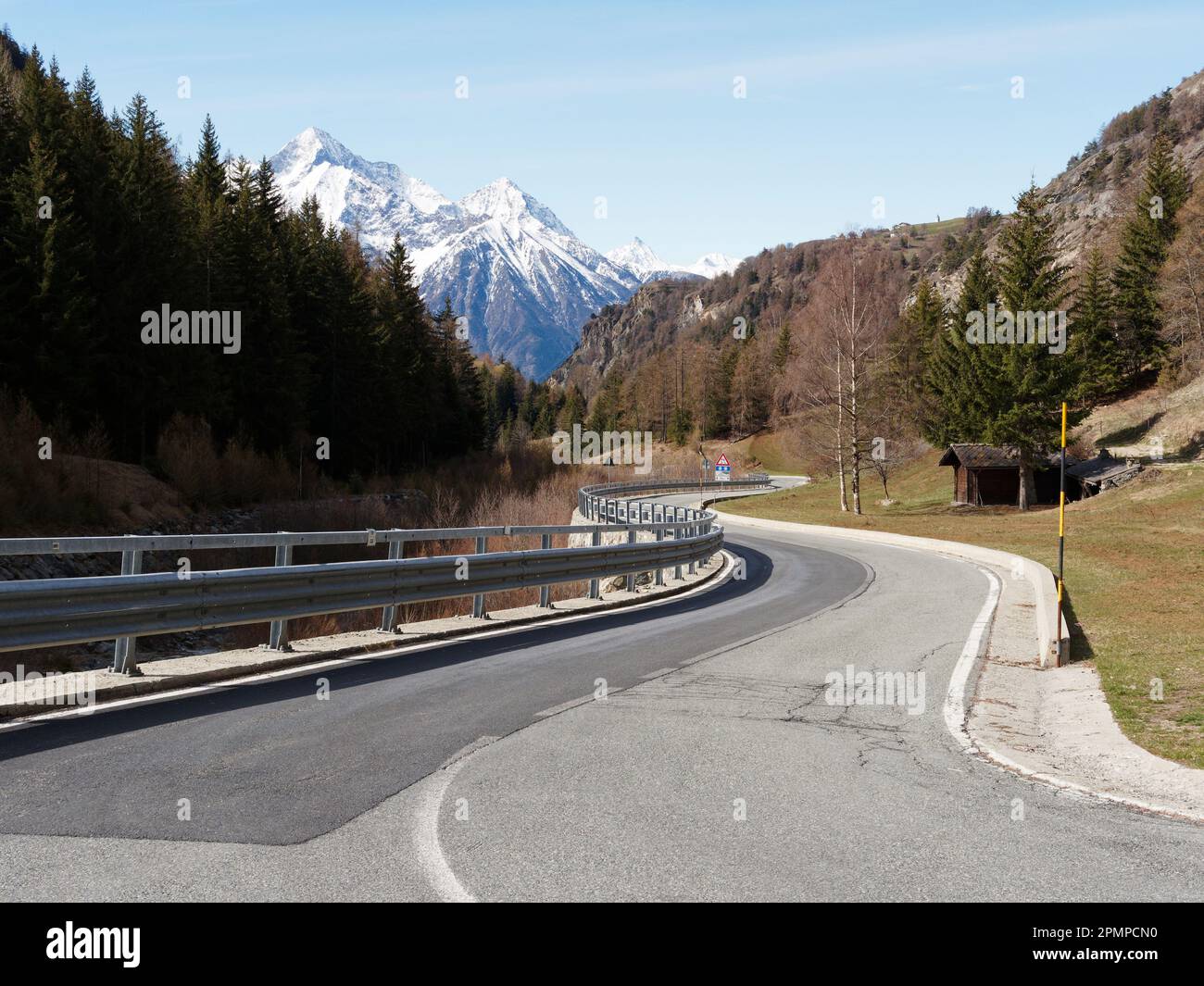 Winding road with forests either side and snow capped alpine mountains ...
