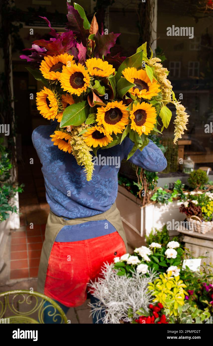 florist entering a shop with a bunch of sunflowers on her shoulder