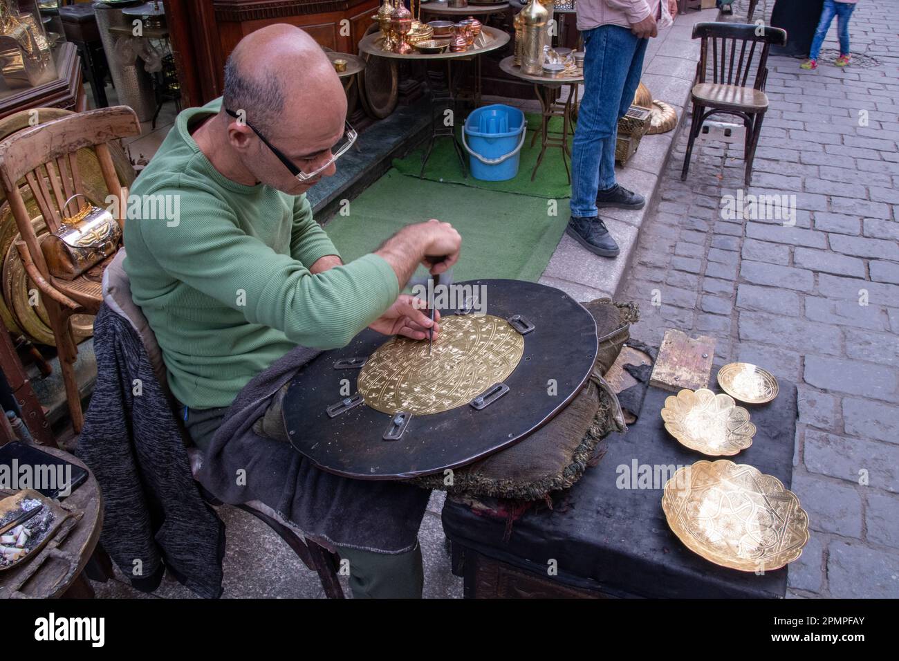 A man carving a gold metal plate to create a bowl in the street market of Khan el-Khalili in Islamic Cairo in Cairo, Egypt Stock Photo