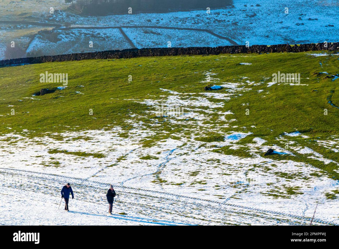 Walkers hiking in a snow covered landscape with trees on the High Peak ...