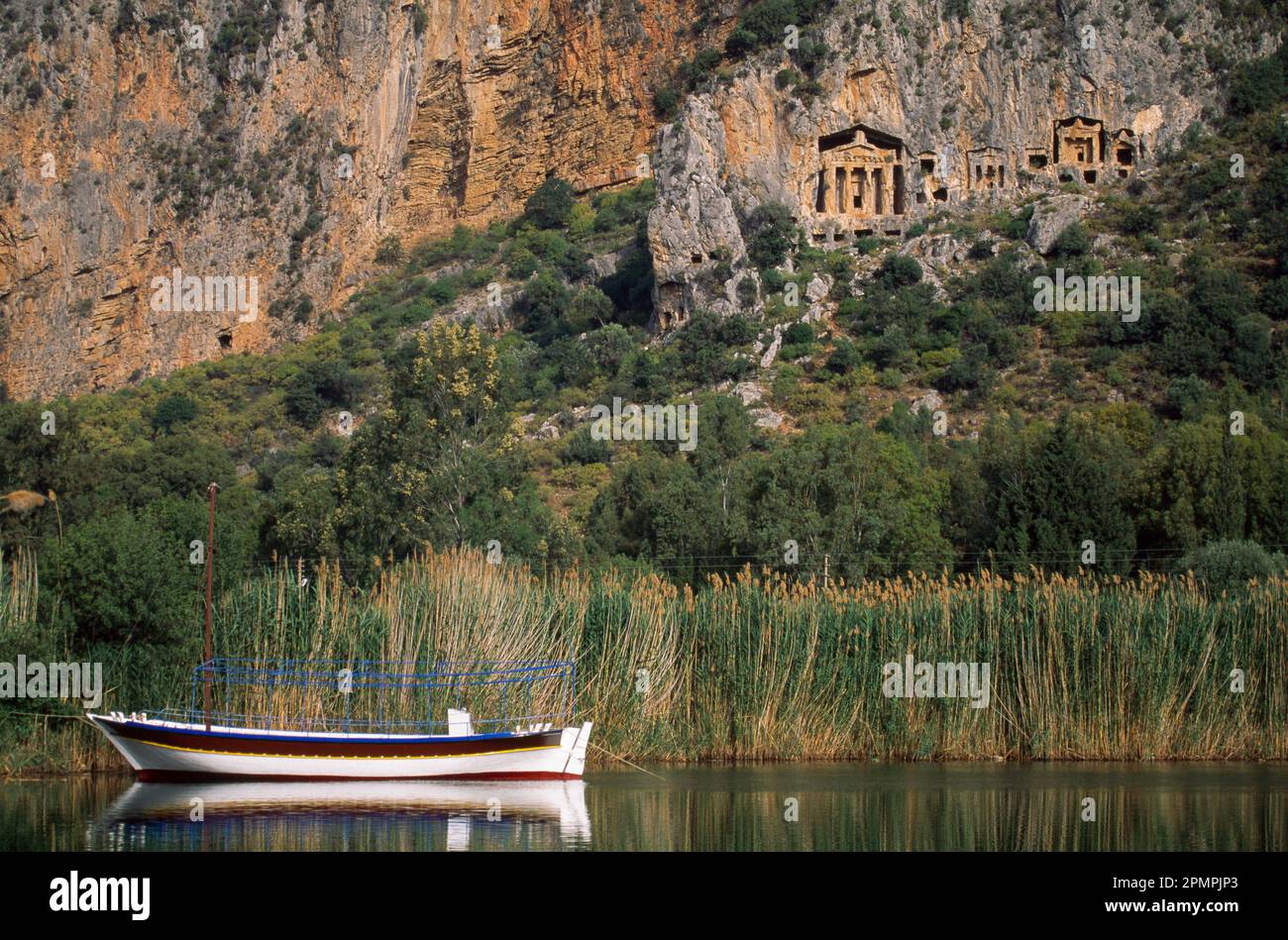 Sailboat anchored in the Dalyan river beneath Lycian rock tombs; Kaunos, Turkey Stock Photo