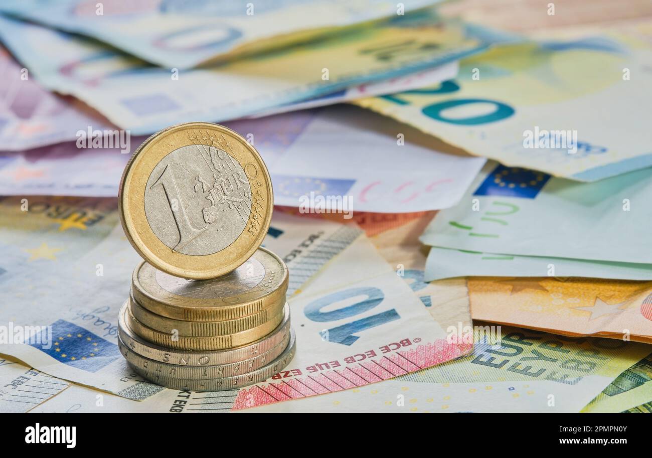 One euro coin on the edge on a stack of coins against the background of banknotes the currency of the European Union. Business finance concept, busine Stock Photo