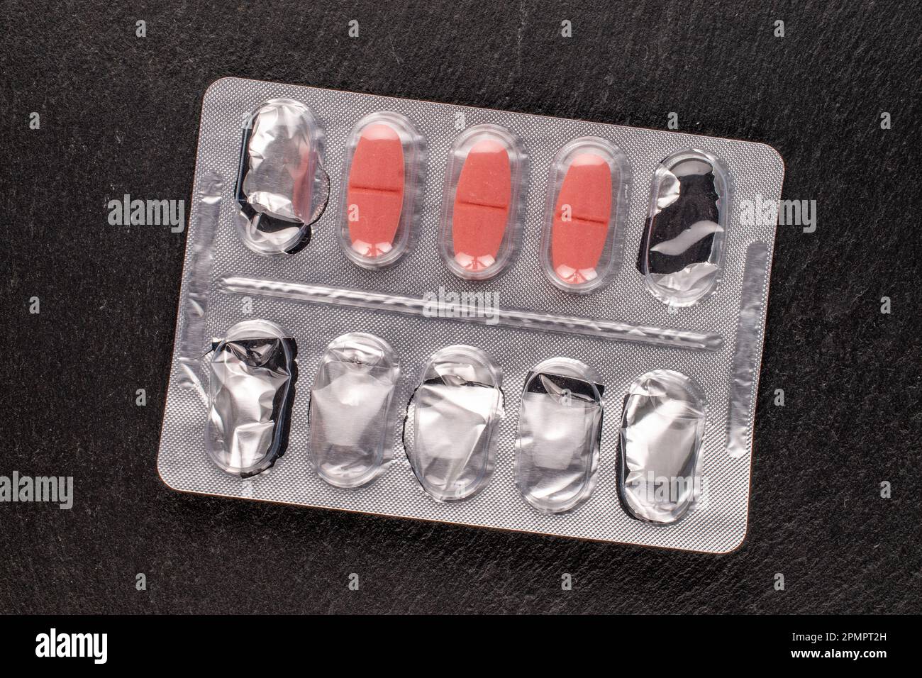 Several medical pills in blister pack on slate stone, macro, top view. Stock Photo