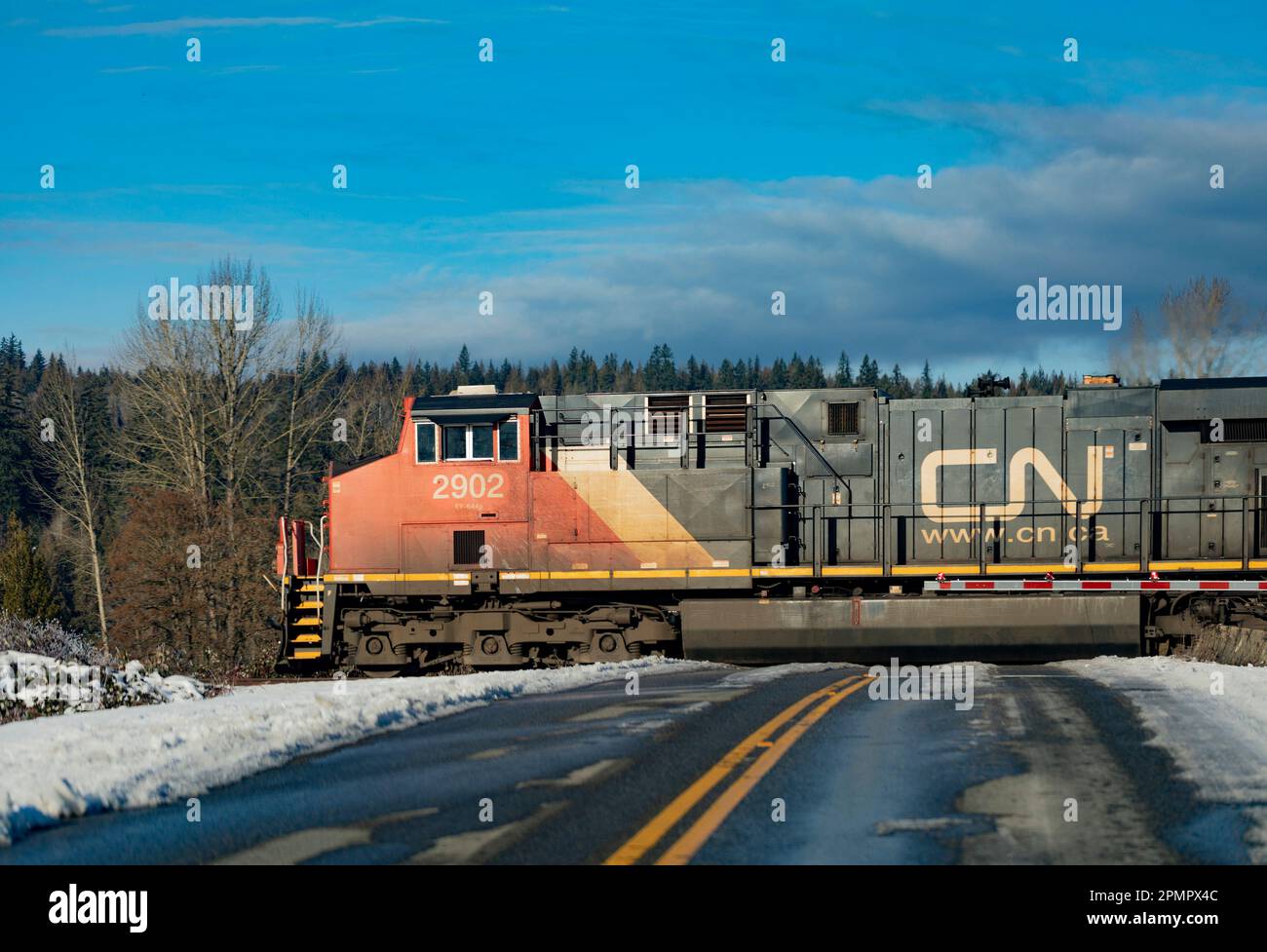 Canadian National Railway train engine on tracks over a road with snow on the roadside; Langley, British Columbia, Canada Stock Photo