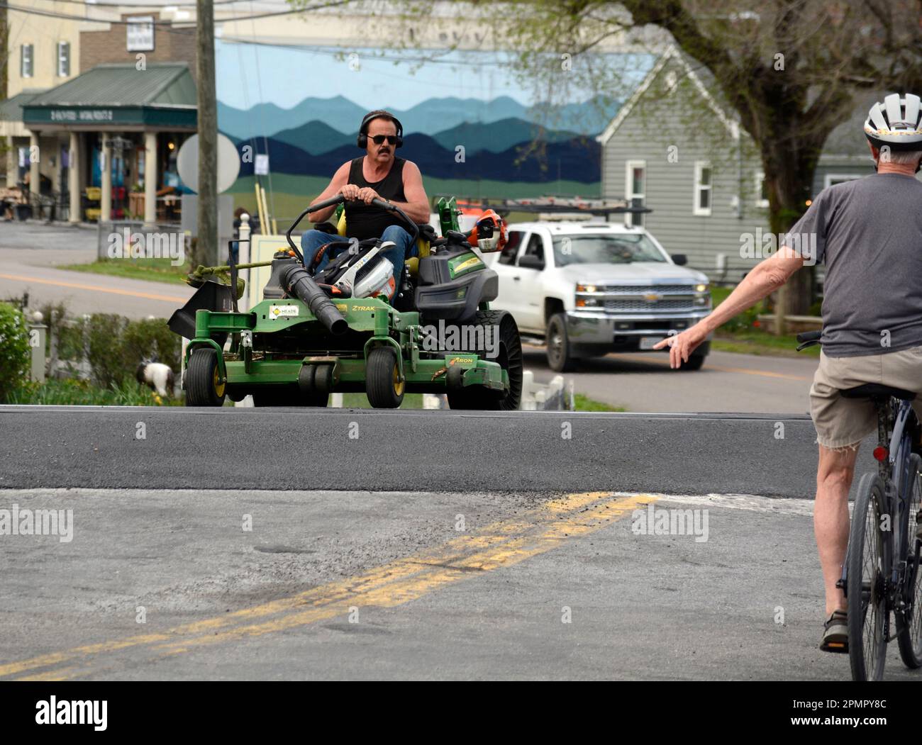 A man rides a John Deere Z970R riding lawn mower on a street in