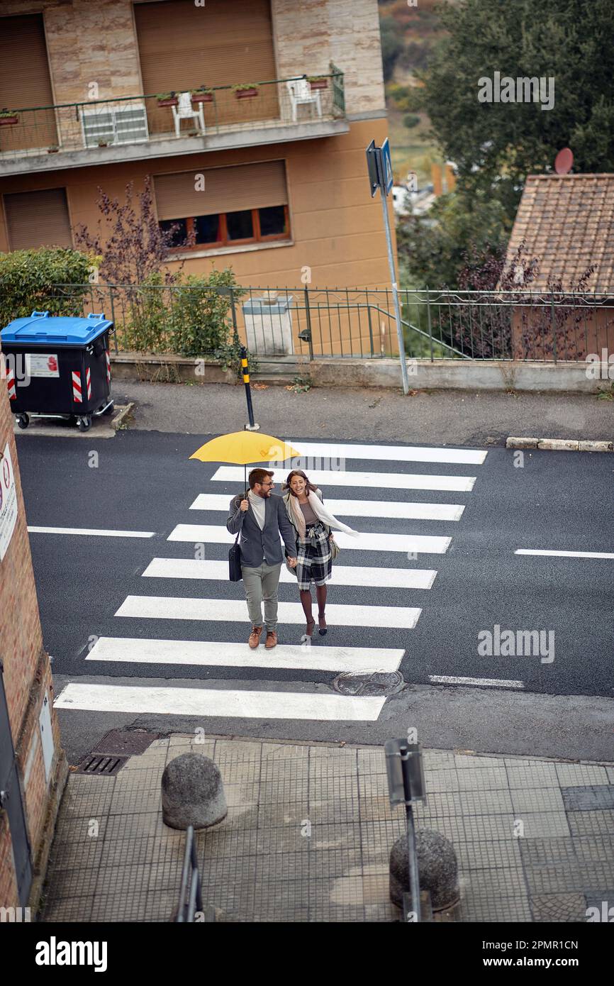 Bird-eye view of a young couple in love is chatting while crossing crosswalk in a good mood during a rainy day. Walk, rain, city, relationship Stock Photo