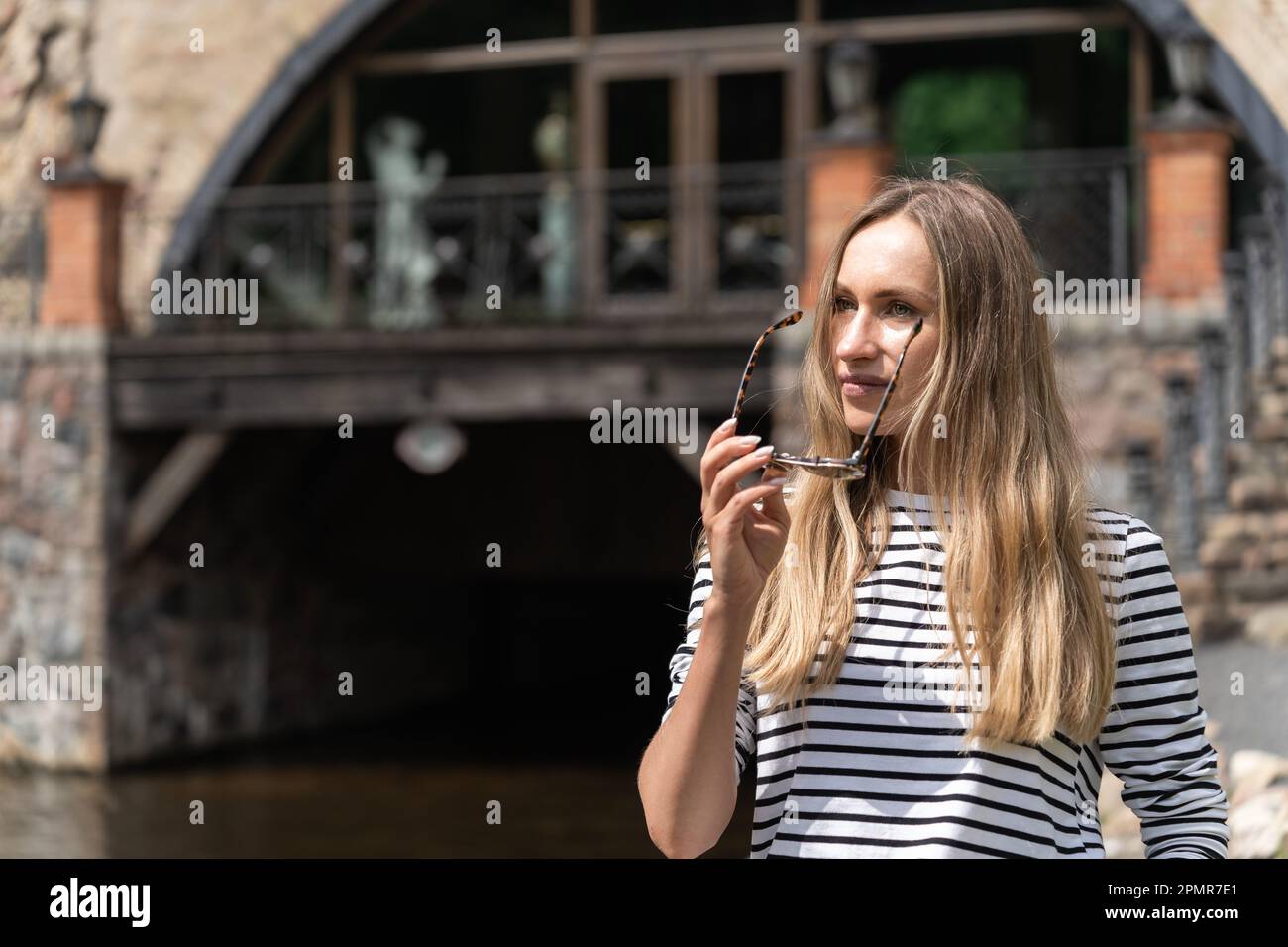 Long-haired woman takes off her sunglasses looking away. Stock Photo
