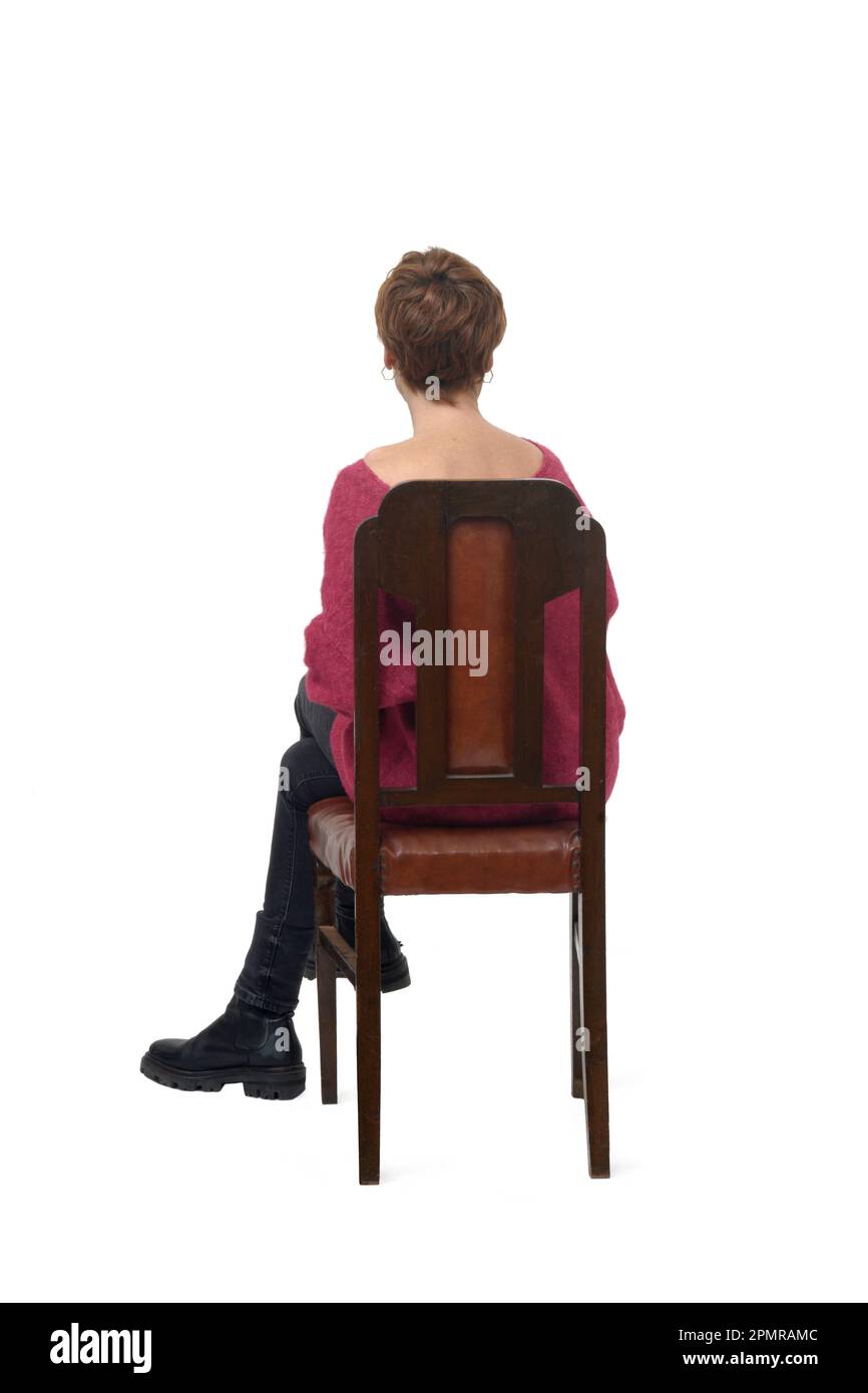 back view of a woman in tight jean pants sitting on chair cross legged on white background Stock Photo