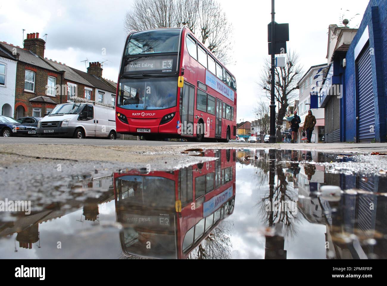 A E3 LONDON BUS IS REFLECTED INA PUDDLE ON NORTHFIRLDS AVE, EALING WEST LONDON. Stock Photo