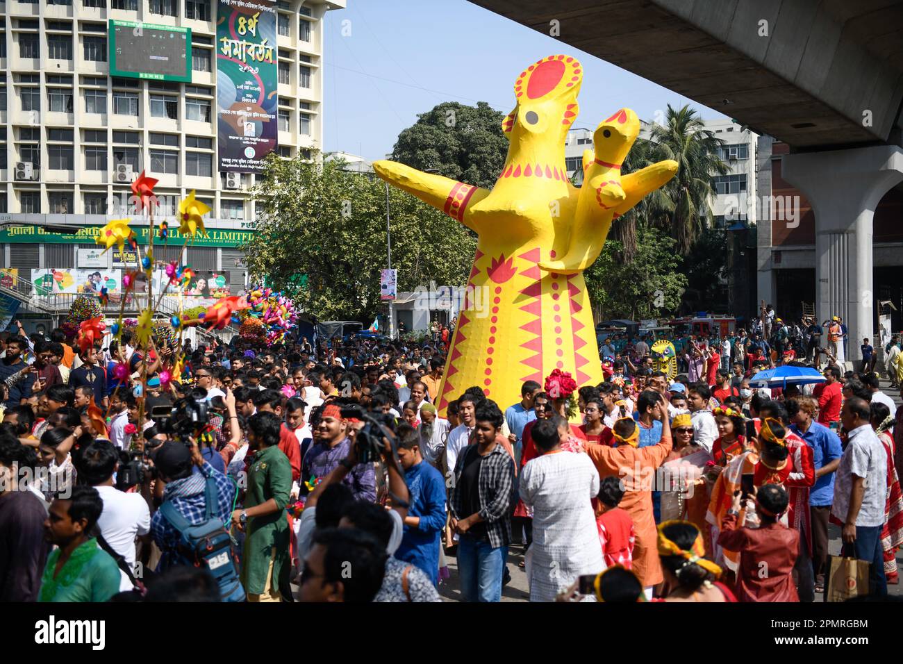 Bangladeshi people participate in a colorful rally with a cartoon of a