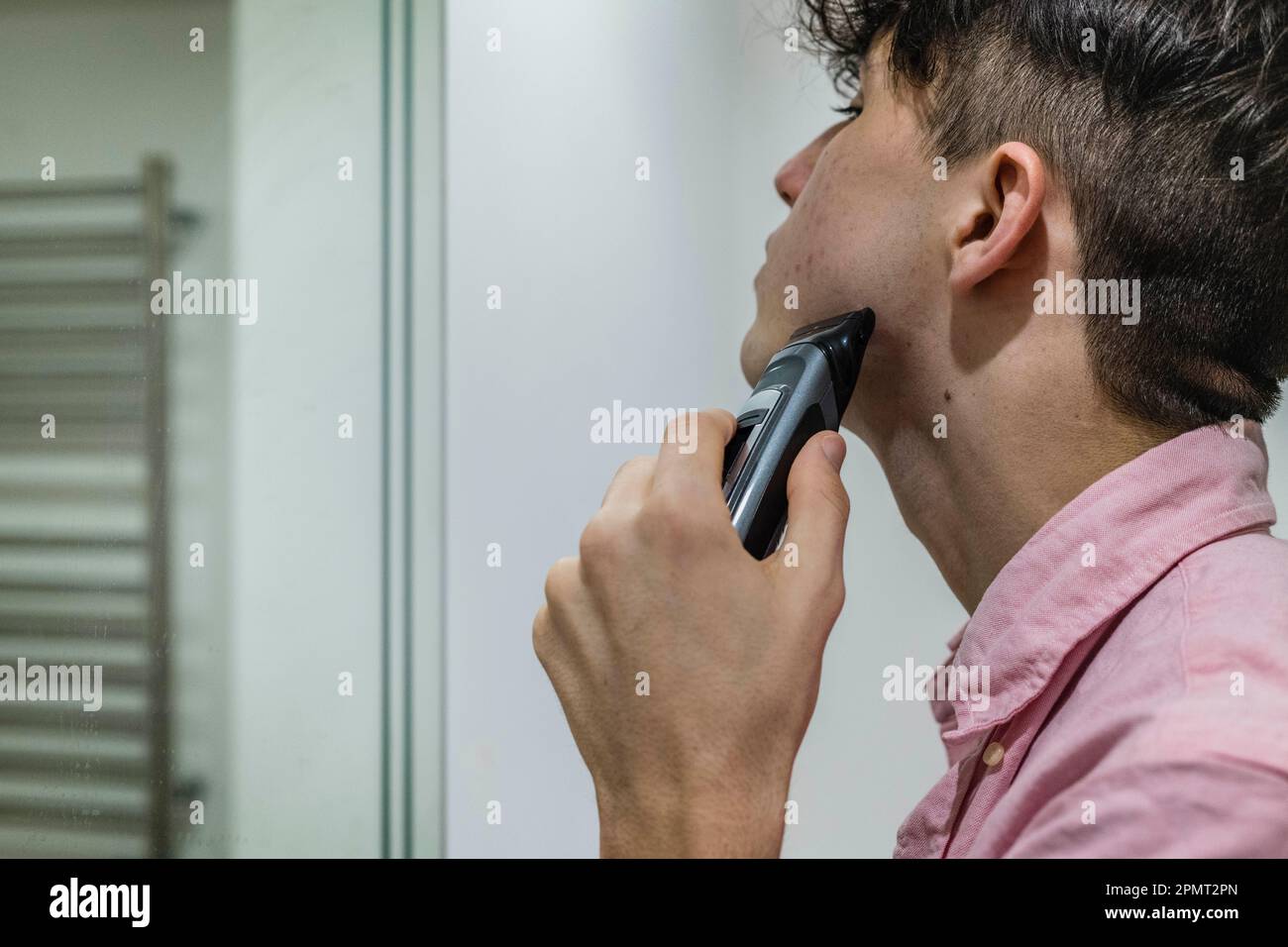 Teenager shaving, focused and looking into Mirror Stock Photo