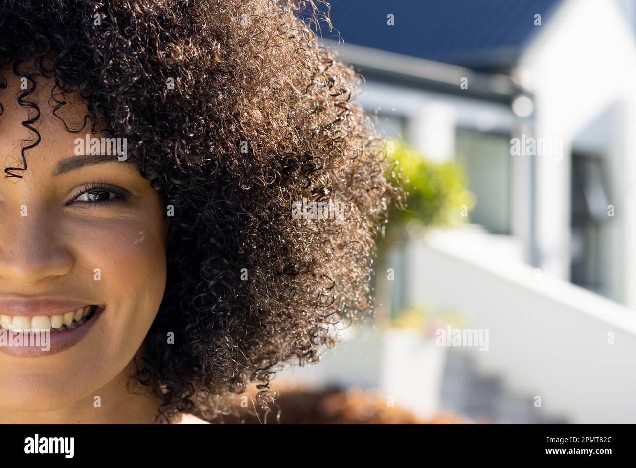 Half face portrait of happy biracial woman smiling and looking to camera in sunny garden, copy space Stock Photo