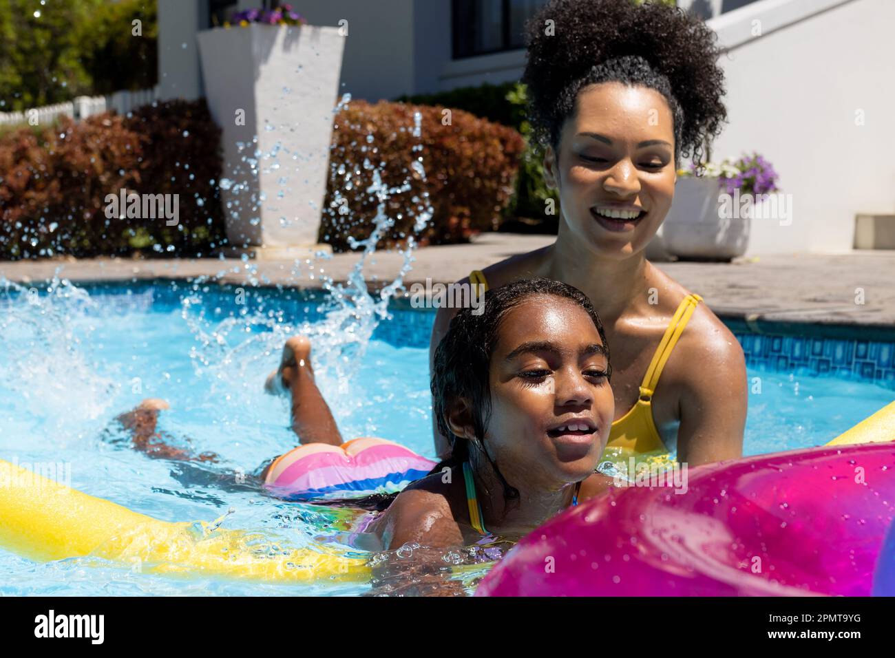 Happy Biracial Mother And Daughter Learning To Swim With Inflatable In Swimming Pool In Garden