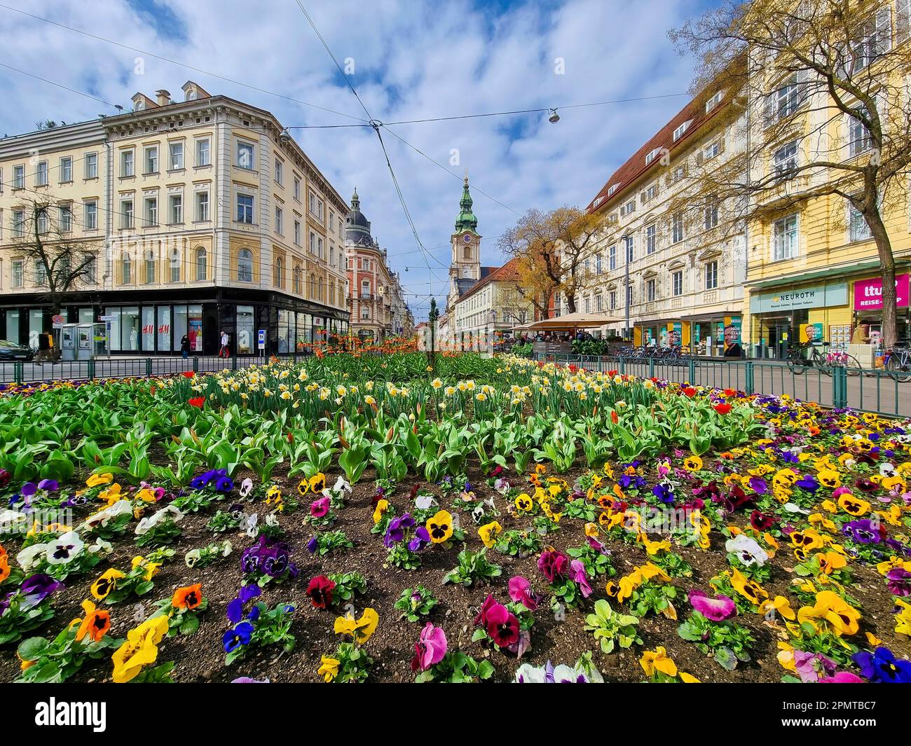Graz, Austria - 26.03.2023: Colorful spring flowers in Jakominiplatz Square and Parish Church in the background, famous attraction in the city of Graz Stock Photo