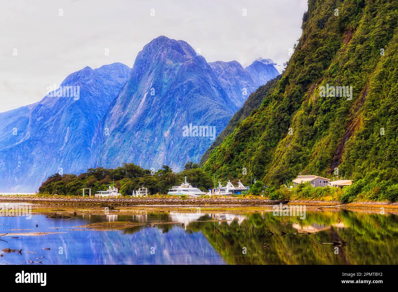 Milford Sound cruise boats passenger tourism terminal under tall mountain peak - South Island of New Zealand. Stock Photo