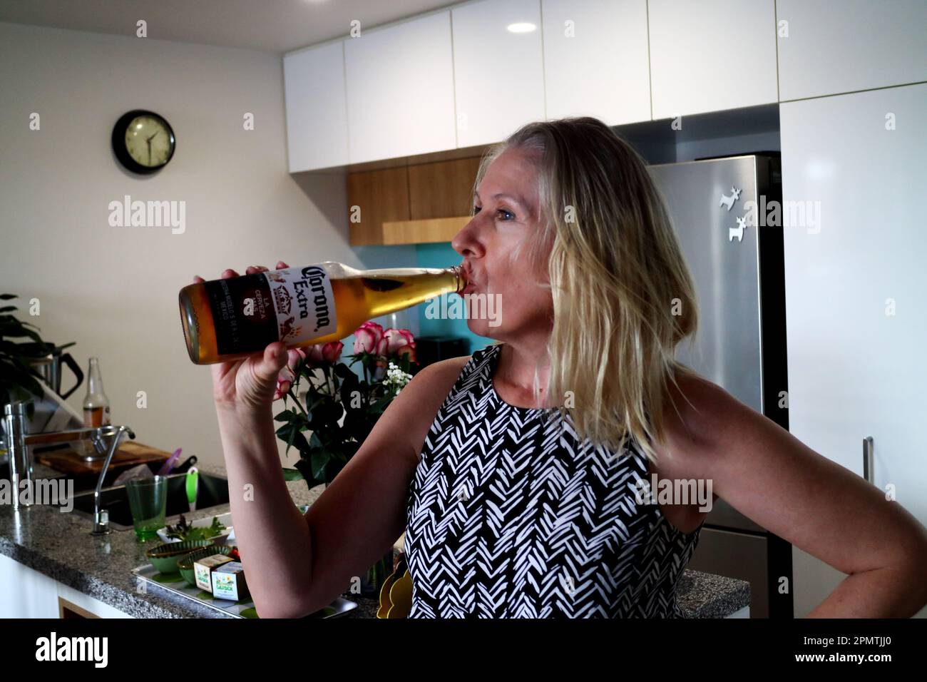Blonde woman drinking huge Corona beer in the kitchen Stock Photo