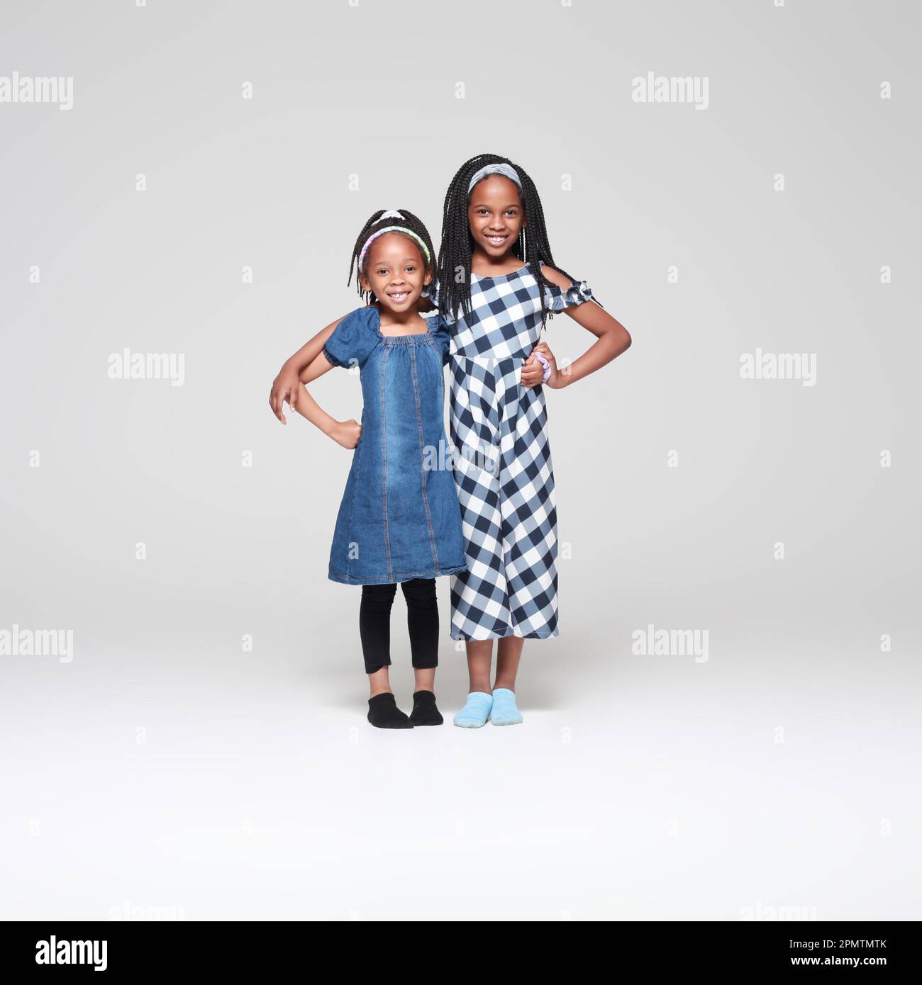 Two beautiful African-American girls with intricate braids pose confidently in a minimalist studio setting, embracing their culture and sisterhood. Stock Photo